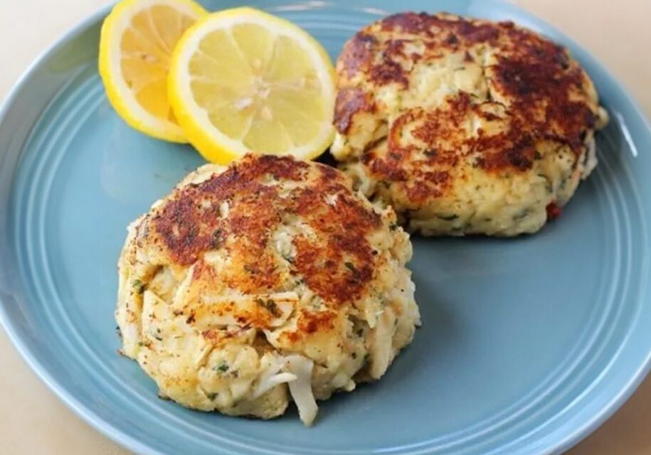 Two crab cakes on a blue plate with lemon wedges.